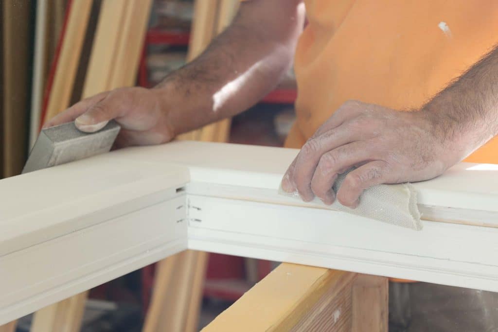 nahaufnahme von einem produktionsmitarbeiter wie er einen Fensterrahmen schleift